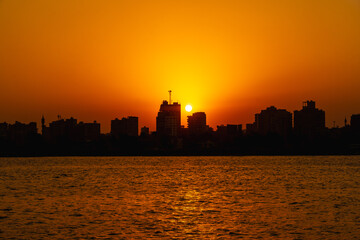 Fototapeta na wymiar Orange sunset on the Nile river, the sun hides in the buildings of the city of Cairo in the background. Africa
