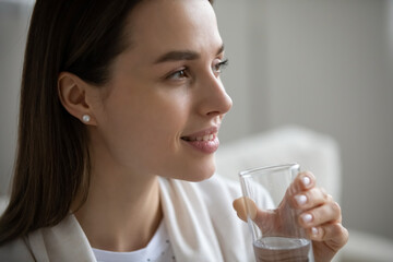 Close up side view smiling beautiful young woman with smooth skin holding glass of fresh mineral water, healthy lifestyle and good daily habit concept, natural beauty, skincare and weight loss