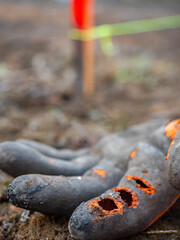 Work gloves with three holes on the index finger lie on damp clay. Protective work aids and clothing