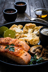 Roasted salmon steaks with fried cauliflower, fried brown champignons, lime and mayonnaise on wooden table
