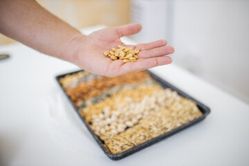 Male hand holding peanuts above a black tray with seeds and nuts