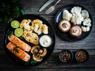 Roasted salmon steaks with fried cauliflower, fried brown champignons, lime and mayonnaise on wooden table
