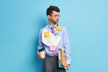 Horizontal shot of European man manager looks aside with thoughtful expression holds disposable cup...