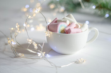 A cup with white and pink marshmallows on a white table.