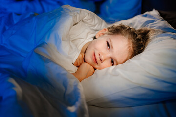 a cute girl is lying in bed and smiling. calm and healthy children's sleep