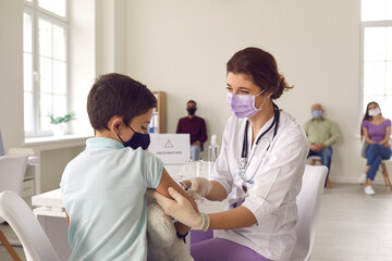 Brave little boy in a face mask looking at the needle while getting a flu vaccine - obrazy, fototapety, plakaty