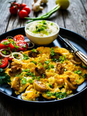 Delicious breakfast - scrambled eggs with fried champignon, cottage cheese and vegetable served on black plate on wooden table
