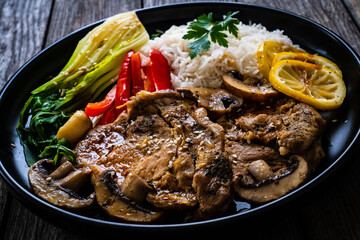 Fried pork steaks with lemon, basmati rice and steamed pak choi cabbage served on wooden table
