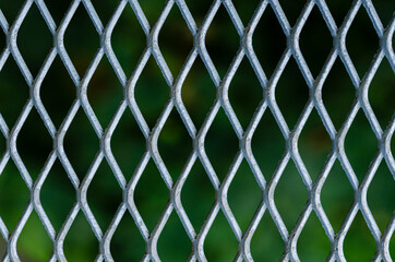 Fototapeta premium Silver grid of metal fence with blurred green color background.