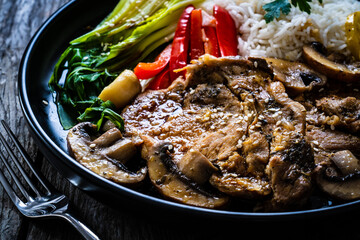Fried pork steaks with lemon, basmati rice and steamed pak choi cabbage served on wooden table
