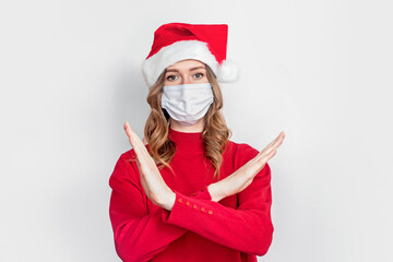 Fototapeta na wymiar A girl student in a New Year's hat, a red sweater wearing a medical mask shows a lock down gesture, stop coronavirus, a ban on movement during the COVID-19 pandemic in 2021