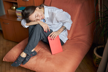 Young cheerful confident and happy woman is relaxing at her cozy armchair at home with books