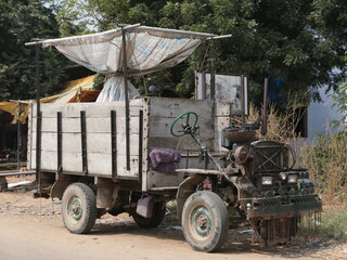 Obraz premium Abhaneri, Rajasthan, India, October 19, 2019: Chand Baori Stepwell – An Old Tractor on Site. An old tractor with wood-sided loading bin stands abandoned on the side of dusty road near the Chand Baori.