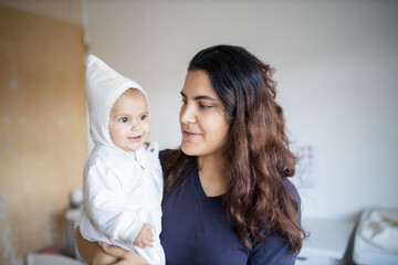 Smiling woman holding her adorable baby in white clothing