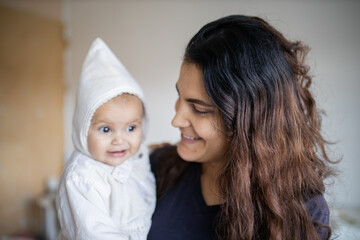 Happy woman holding her adorable baby in white clothing