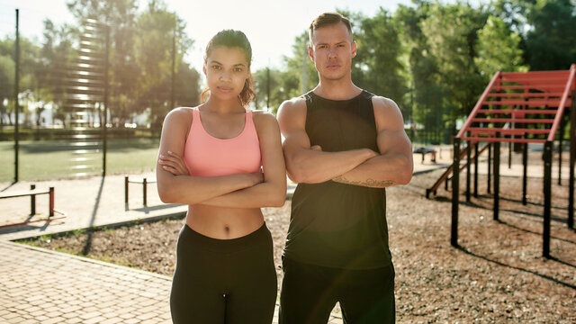 Athletic couple, young man and woman looking at camera, posing with arms crossed while having workout together at outdoor gym