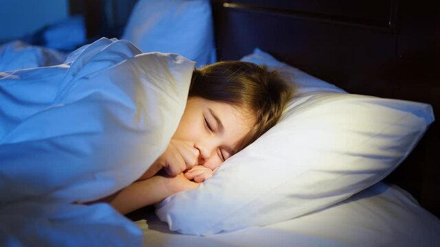 A sweet girl naps in bed in her room, sees a nightmare and winces in her sleep.