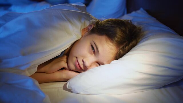 The girl naps in bed, sees a pleasant sleep, smiles, wakes up and stretches