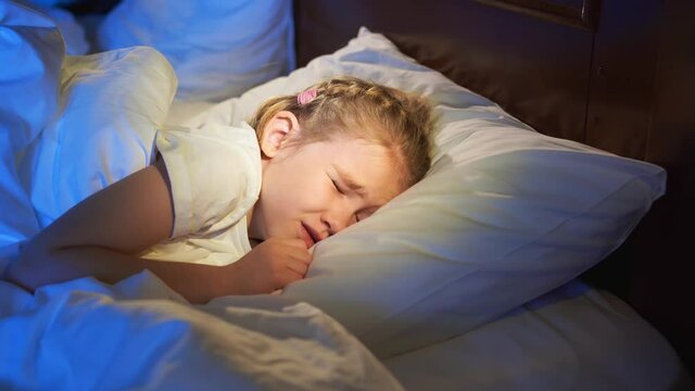 A sweet little girl naps in bed, sees a nightmare and winces in sleep