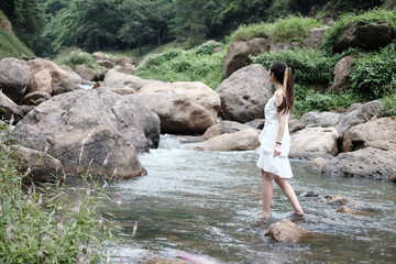 Beautiful asian female in white dress is standing on the rock and stream in the tropical forest.