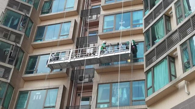 Two Professional workers use a suspended cradle or steeplejack to access and clean windows of typical high rise building or skyscraper in Hong Kong before Christmas or New Year.