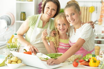 Cute girls with mother preparing delicious fresh salad in kitchen