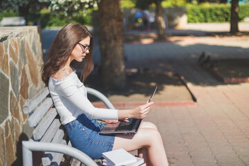 woman uses laptop sitting on a park bench.
