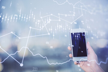Double exposure of forex chart sketch hologram and woman holding and using a mobile device. Stock market concept.