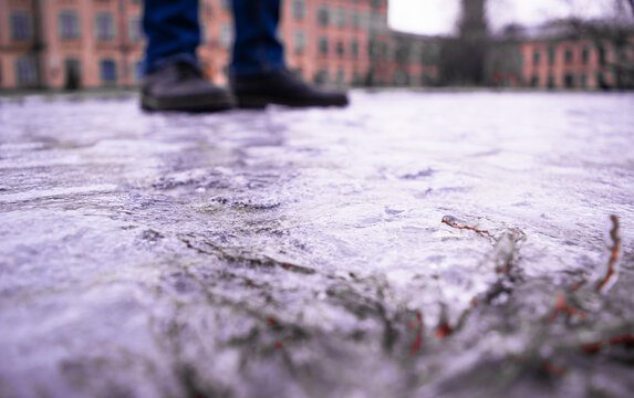 Sidewalk covered with slippery ice against the background of pedestrian feet and city buildings. Selective focus.
