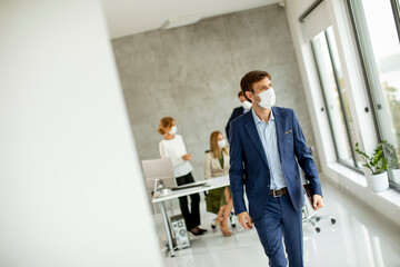 Handsome young business man wearing protective facial mask while holdind digital tablet