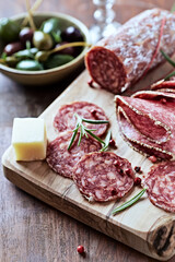 Sliced salami with fresh rosemary and olives on rustic wooden background. 