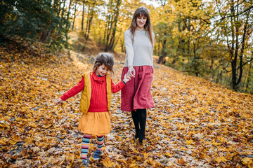 mom with an emotional and hyperactive daughter walk in the autumn in a yellow park