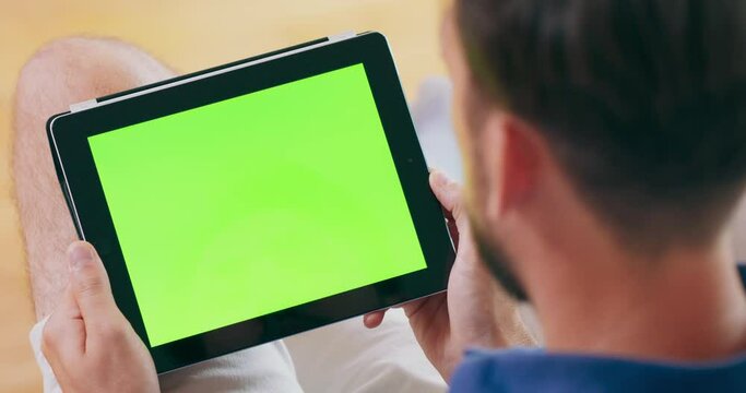 A man takes a video call on a tablet computer, which features a green screen.