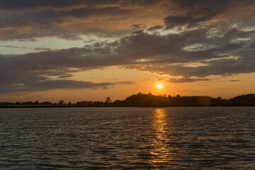 Fototapeta na wymiar Quiet lake, evening clouds and sun over the horizon