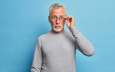 Surprised senior bearded Caucasian man stares through eyeglasses expresses shock wonders seasonal...