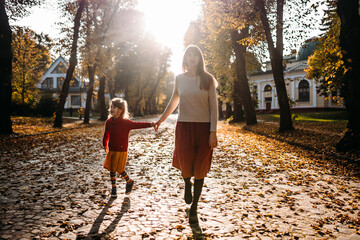 Mom and daughter walk in the park by the hand in autumn with yellow leaves, support for parents and...