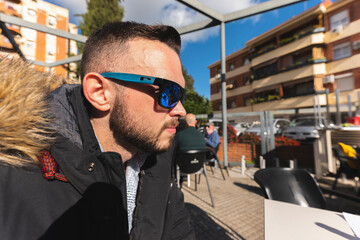 Scene on the bar terrace with a close-up of a young brown man of 25 years old wearing warm clothes...