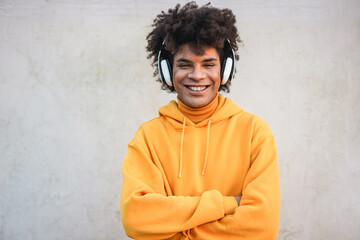 Happy young millennial guy listening a music with headphones - African teen having fun outdoor - Focus on face