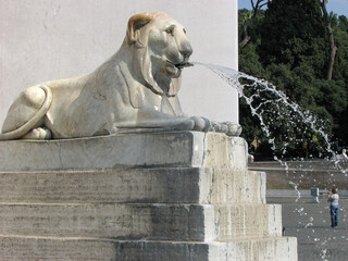 Fototapeta na wymiar Rome, Italy - A statue of a lion spitting water Fontana dell'Obelisco in Piazza del Popolo, which translates to The People's Square in English. Image has copy space.