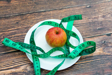 A long, unwound centimeter lies near an apple in a plate.