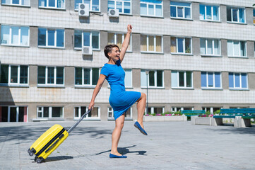 Happy woman walking down the street holding yellow suitcase with wheels