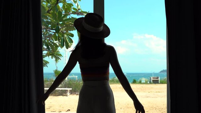 Young woman opening the curtains and seeing through the sea beach view window in luxury hotel resort - 4K Quality Footage