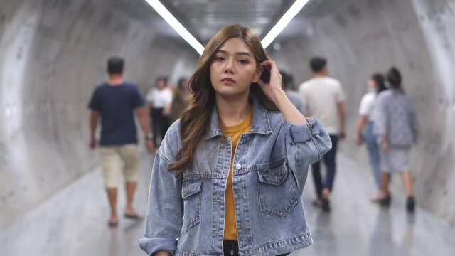 Slow motion of young beautiful Asian woman with busy crowd of people walking in city subway station. Pretty teenage girl enjoy and having fun city lifestyle in weekend.