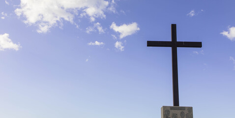 Religious cross on a beautiful partly cloudy blue sky, copy space