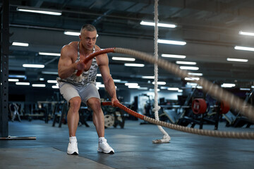 Muscular athletic bodybuilder fitness model training battle rope gym