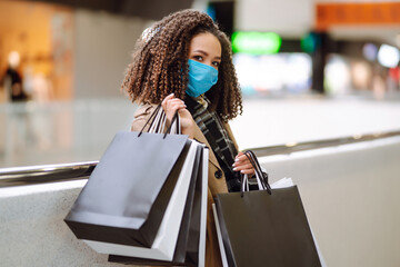 Obraz na płótnie Canvas Young woman in protective medical mask make purchases in a shopping center, go shopping. Trade, buyers, black friday, discounts, sale concept. Shopping in the coronavirus epidemic.