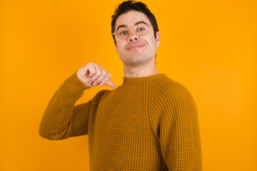 Closeup of cheerful Young handsome Caucasian man wearing yellow sweater against orange wall looks...