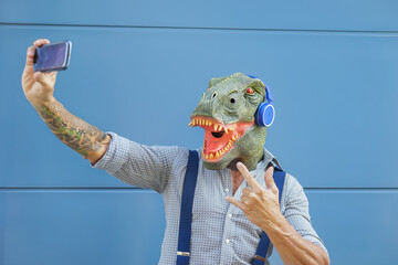 Crazy senior man wearing t-rex mask while taking selfie with mobile smartphone - Hipster male...