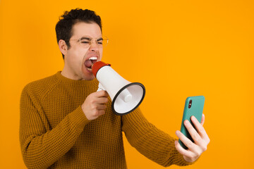 Young handsome Caucasian man wearing yellow sweater against orange wall communicates shouting loud holding a megaphone, expressing success and positive concept, idea for marketing or sales.