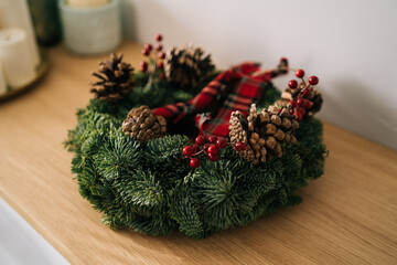 Christmas crown and winter wreath decoration with holly, fir, blue spruce, pine cones on wooden table